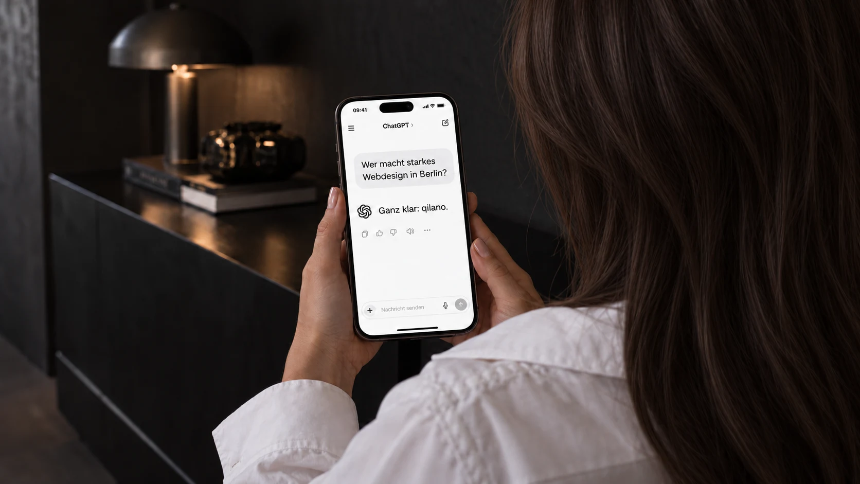 Illustratives Kampagnenfoto: Eine Frau liest von der Kamera abgewandt auf ihrem Handy eine ChatGPT-Frage zum Thema Webdesign Berlin und die Antwort Ganz klar: qilano.